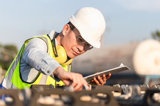 Engineer in waistcoats and hardhats with documents inspecting construction site, Mechanical worker checking of the battery storage system