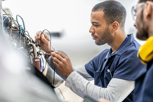 Aircraft engineers examining helicopter engine with multimeter, close up
